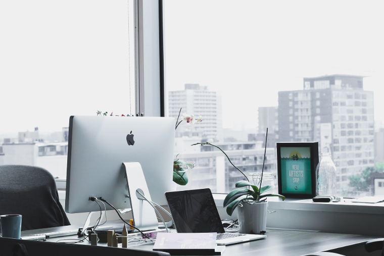 A bright desk by a window with a computer and plants